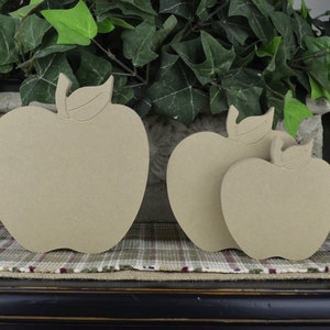 May include: Three unfinished wooden apple shapes of varying sizes. The apples are all beige in color and have a simple, classic design.