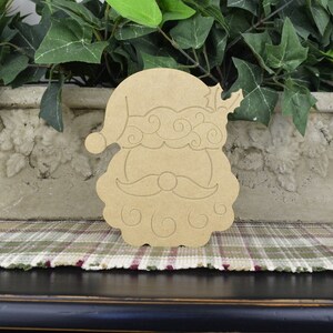 May include: Unfinished wooden cutout of Santa Claus's face with a curly beard and a hat. The cutout is a light brown color and has a simple design.
