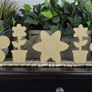 May include: Five unfinished wooden flower shapes, including four individual flowers and one flower in a pot. The flowers are all different shapes and sizes, and they are all made of a light brown wood.