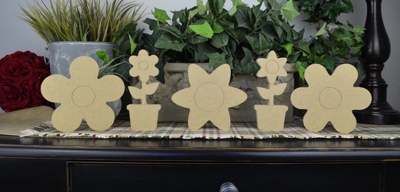 May include: Five unfinished wooden flower shapes, including four individual flowers and one flower in a pot. The flowers are all different shapes and sizes, and they are all made of a light brown wood.