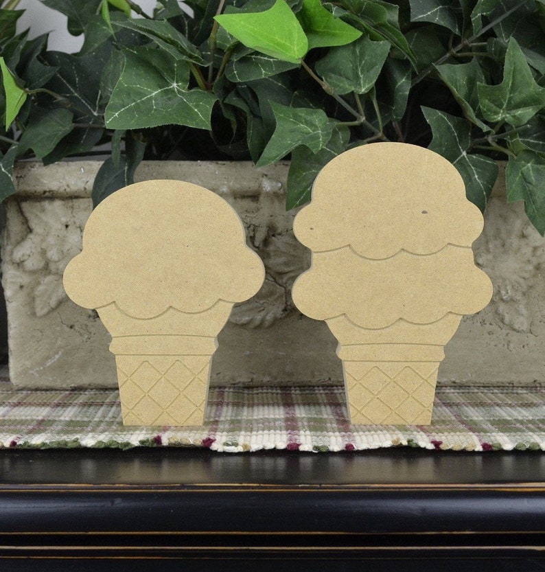 May include: Two wooden ice cream cone shapes, one with a single scoop and the other with two scoops. The cones are textured to look like waffle cones.