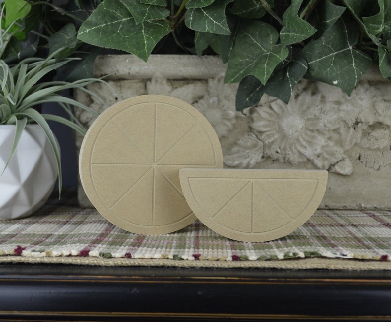 May include: Two unfinished wooden craft shapes of a whole lemon and a lemon slice. The shapes are made of a light brown wood and have a textured surface.