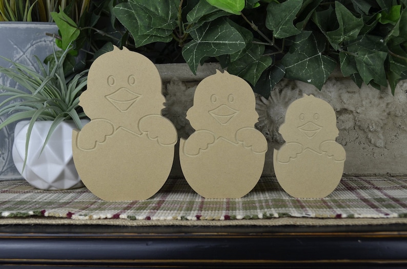 May include: Three wooden cutouts of chicks hatching from eggs. The chicks are in different sizes, with the largest chick being about 6 inches tall. The cutouts are made of unfinished wood and are ready to be painted or stained.