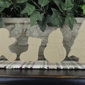 K&ouml;nnte beinhalten: Satz von f&uuml;nf unfertigen Weihnachtsbaumschmuck aus Holz. Der Schmuck ist in Form eines Lebkuchenmanns, eines Strumpfes, eines Schneemanns, eines Weihnachtsbaums und einer Glocke. Der Schmuck ist aus Naturholz gefertigt und kann bemalt oder verziert werden.