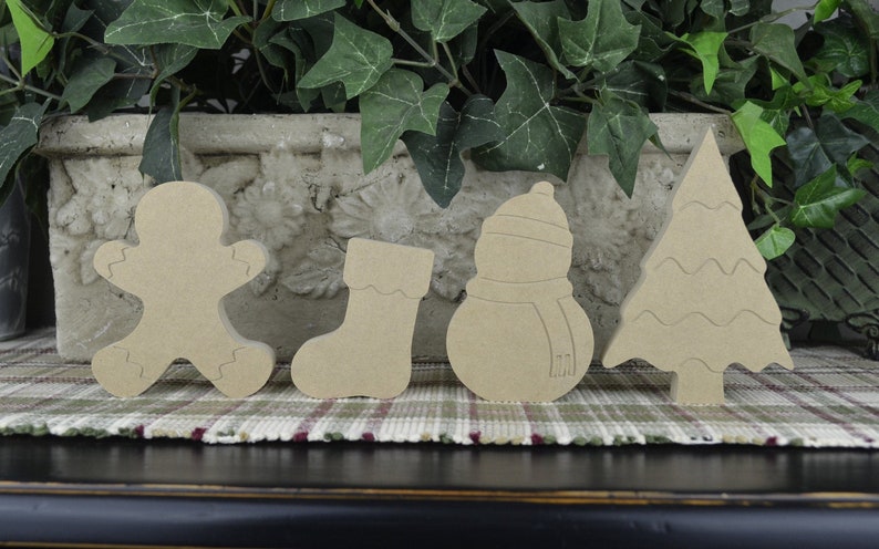 K&ouml;nnte beinhalten: Satz von f&uuml;nf unfertigen Weihnachtsbaumschmuck aus Holz. Der Schmuck ist in Form eines Lebkuchenmanns, eines Strumpfes, eines Schneemanns, eines Weihnachtsbaums und einer Glocke. Der Schmuck ist aus Naturholz gefertigt und kann bemalt oder verziert werden.