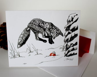 May include: A black and white illustration of a fox leaping towards a red Christmas ornament in the snow. The artwork is on a white card, with a pine cone and envelope visible in the background. A festive holiday card.
