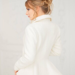 K&ouml;nnte beinhalten: Eine wei&szlig;e, lang&auml;rmelige Jacke mit einem Peplum-Saum und einem hohen Kragen. Die Jacke ist aus einem weichen, strukturierten Stoff gefertigt.
