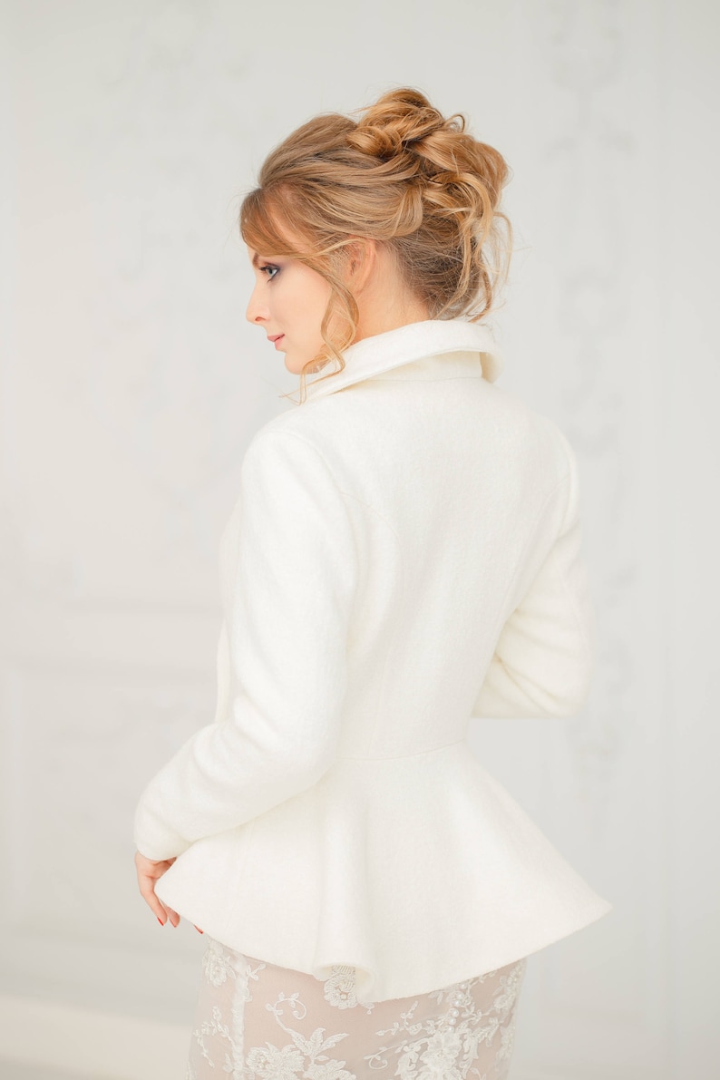 K&ouml;nnte beinhalten: Eine wei&szlig;e, lang&auml;rmelige Jacke mit einem Peplum-Saum und einem hohen Kragen. Die Jacke ist aus einem weichen, strukturierten Stoff gefertigt.