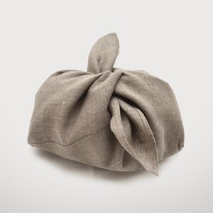 May include: A brown linen fabric pouch tied with a knot at the top. The pouch is made of a natural, unbleached linen and has a rustic, handmade look.