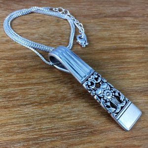 May include: A silver necklace with a pendant made from a vintage silverware piece. The pendant has a floral design and is attached to a silver chain.