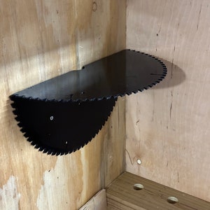 May include: A black circular saw blade repurposed as a shelf, mounted on a wooden wall.