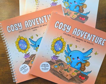 Puede incluir: Varios libros para colorear con espiral y cubiertas naranjas están apilados. La portada presenta un ajolote azul con una lupa, un mapa y el texto "COSY ADVENTURE". Los libros se titulan "COLORIE LES MONDES DE NOLOTL".