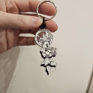 Puede incluir: Un llavero de acr&iacute;lico transparente con una ilustraci&oacute;n en blanco y negro de Mickey Mouse y Minnie Mouse. Mickey sostiene a Minnie en sus brazos y ambos sonr&iacute;en. El llavero est&aacute; unido a un llavero plateado.