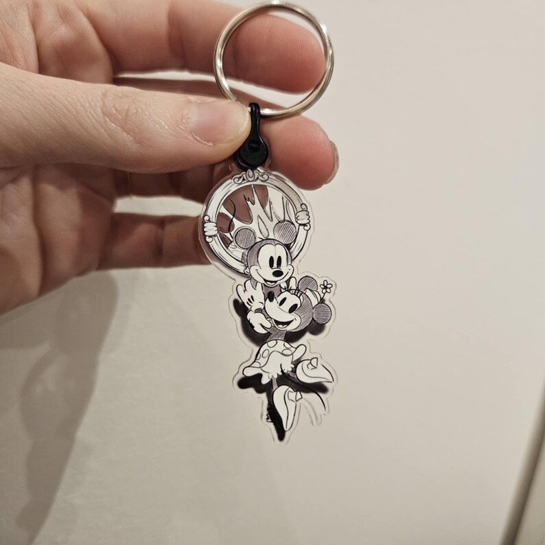 Puede incluir: Un llavero de acr&iacute;lico transparente con una ilustraci&oacute;n en blanco y negro de Mickey Mouse y Minnie Mouse. Mickey sostiene a Minnie en sus brazos y ambos sonr&iacute;en. El llavero est&aacute; unido a un llavero plateado.