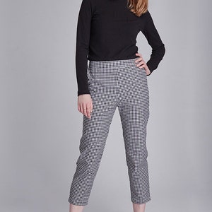 May include: A person wearing a black ribbed long-sleeve shirt and black and white checkered cropped pants. The person is also wearing brown leather loafers. The background is a solid gray.
