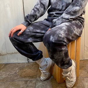 Könnte beinhalten: Eine Person trägt eine schwarze und weiße Tie-Dye-Jogginghose und ein passendes Sweatshirt. Sie trägt weiße Turnschuhe mit schwarzen Akzenten.
