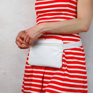 May include: A white fanny pack with a zipper closure worn over a red and white striped dress.