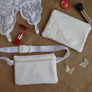 May include: A collection of white accessories and makeup items on a textured brown surface. Includes a white lace garter, a white zippered pouch with lace detailing, a white fanny pack, red lipstick, blush, a makeup brush, and butterfly earrings.