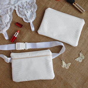 May include: A white lace suspender belt, two red lipsticks, a white makeup bag, a white fanny pack with a white strap, and two gold butterfly earrings on a brown hessian background.