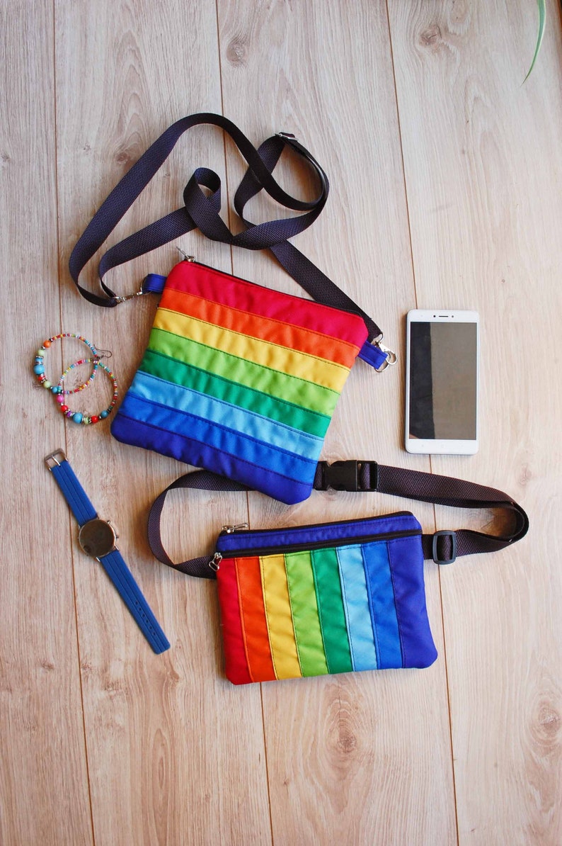 May include: Two rainbow striped fabric bags with black adjustable straps. One bag is a crossbody style and the other is a fanny pack.