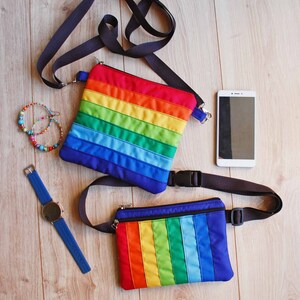 May include: Two rainbow striped fabric bags with black straps. One bag is a crossbody bag and the other is a fanny pack.