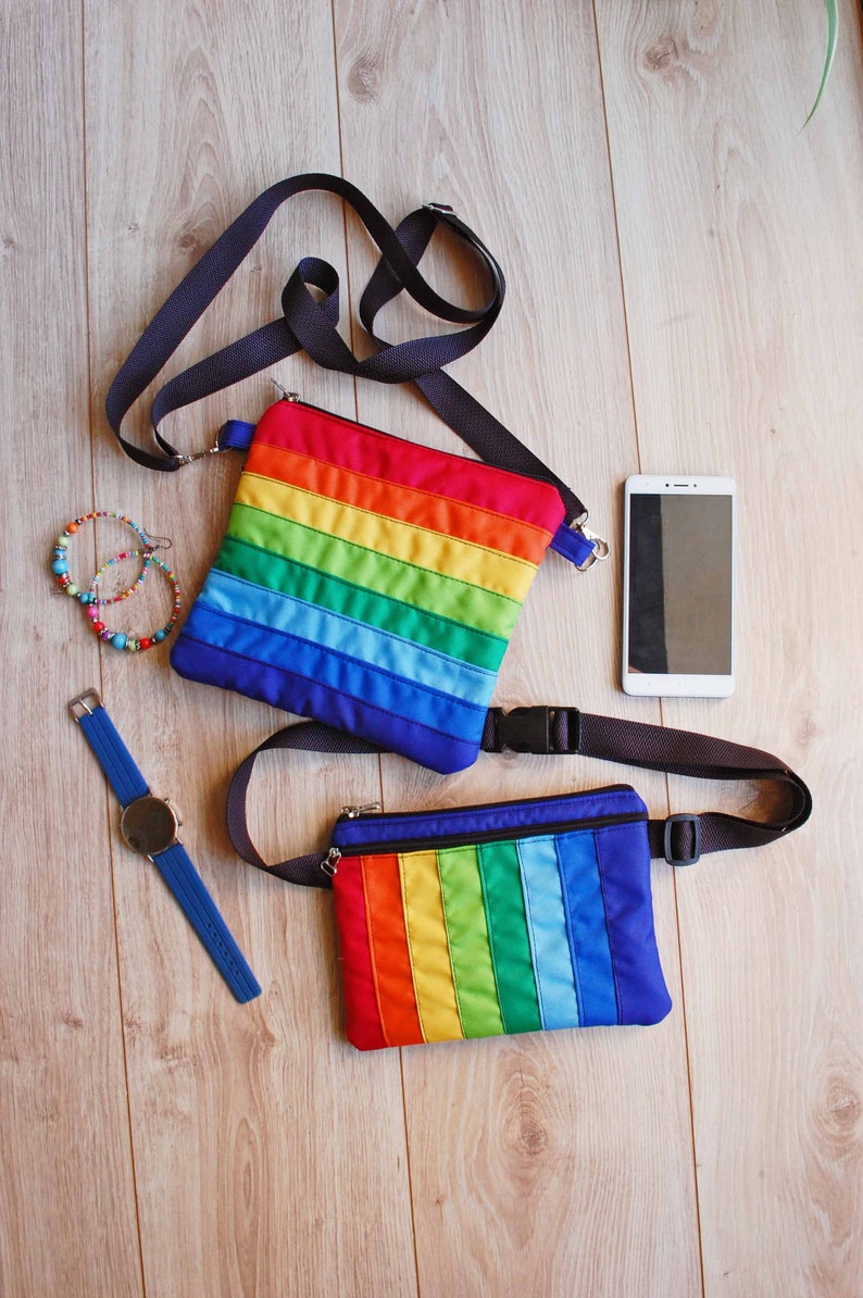 May include: Two rainbow striped fabric bags with black straps. One bag is a crossbody bag and the other is a fanny pack.