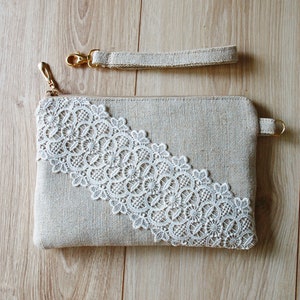 May include: A beige clutch bag with a white lace trim and a gold zip. The bag has a matching beige strap with a gold clasp.