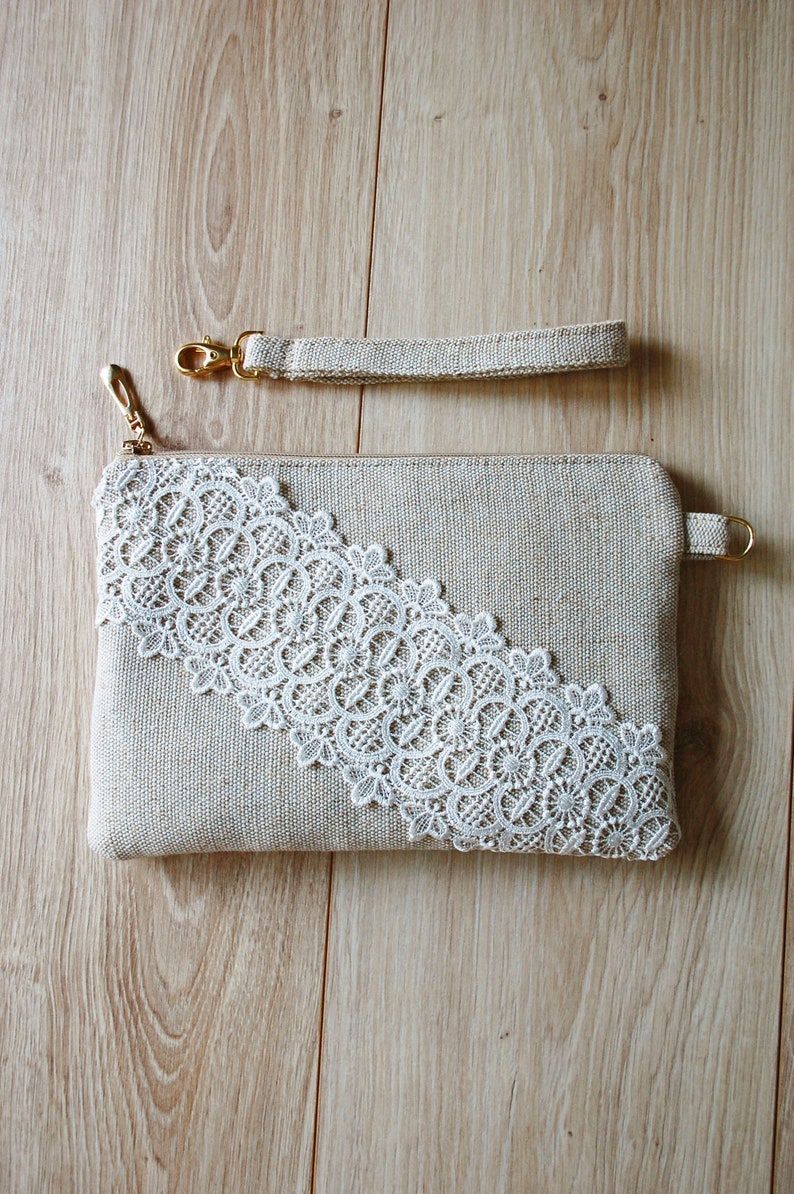 May include: A beige clutch bag with a white lace trim and a gold zip. The bag has a matching beige strap with a gold clasp.