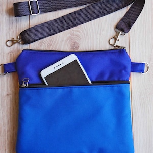 May include: A blue and red crossbody bag with a zippered pocket and a black adjustable strap. A white smartphone is in the pocket.