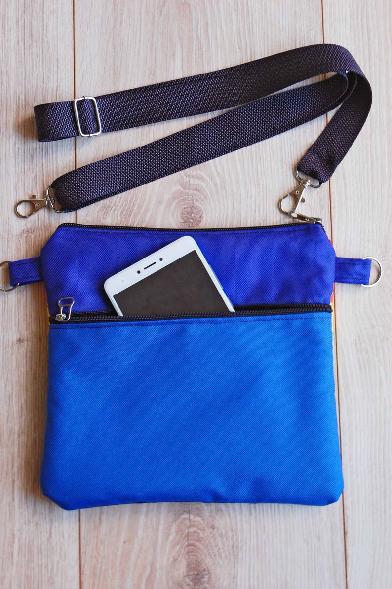 May include: A blue and red crossbody bag with a zippered pocket and a black adjustable strap. A white smartphone is in the pocket.