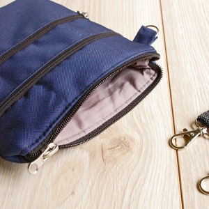 May include: A small blue zippered pouch with two zippered compartments. The pouch is open and the inside is lined with a light gray fabric.