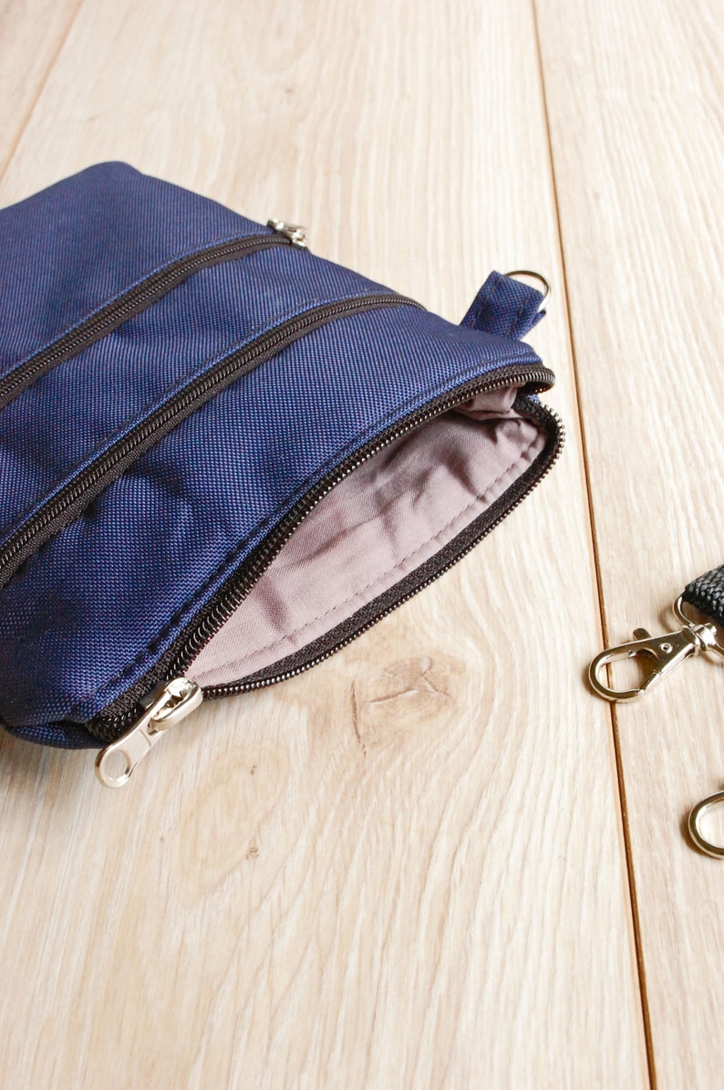May include: A small blue zippered pouch with two zippered compartments. The pouch is open and the inside is lined with a light gray fabric.