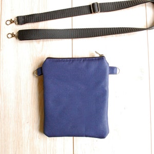 May include: A small, dark blue zippered pouch with a black adjustable strap. The pouch is made of a soft, fabric material.