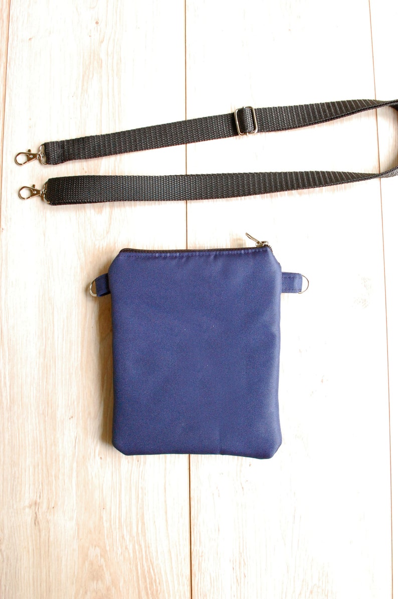 May include: A small, dark blue zippered pouch with a black adjustable strap. The pouch is made of a soft, fabric material.