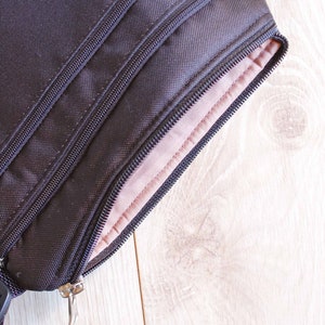 May include: A black zippered pouch with a brown lining. The pouch has a zipper pull and a strap.