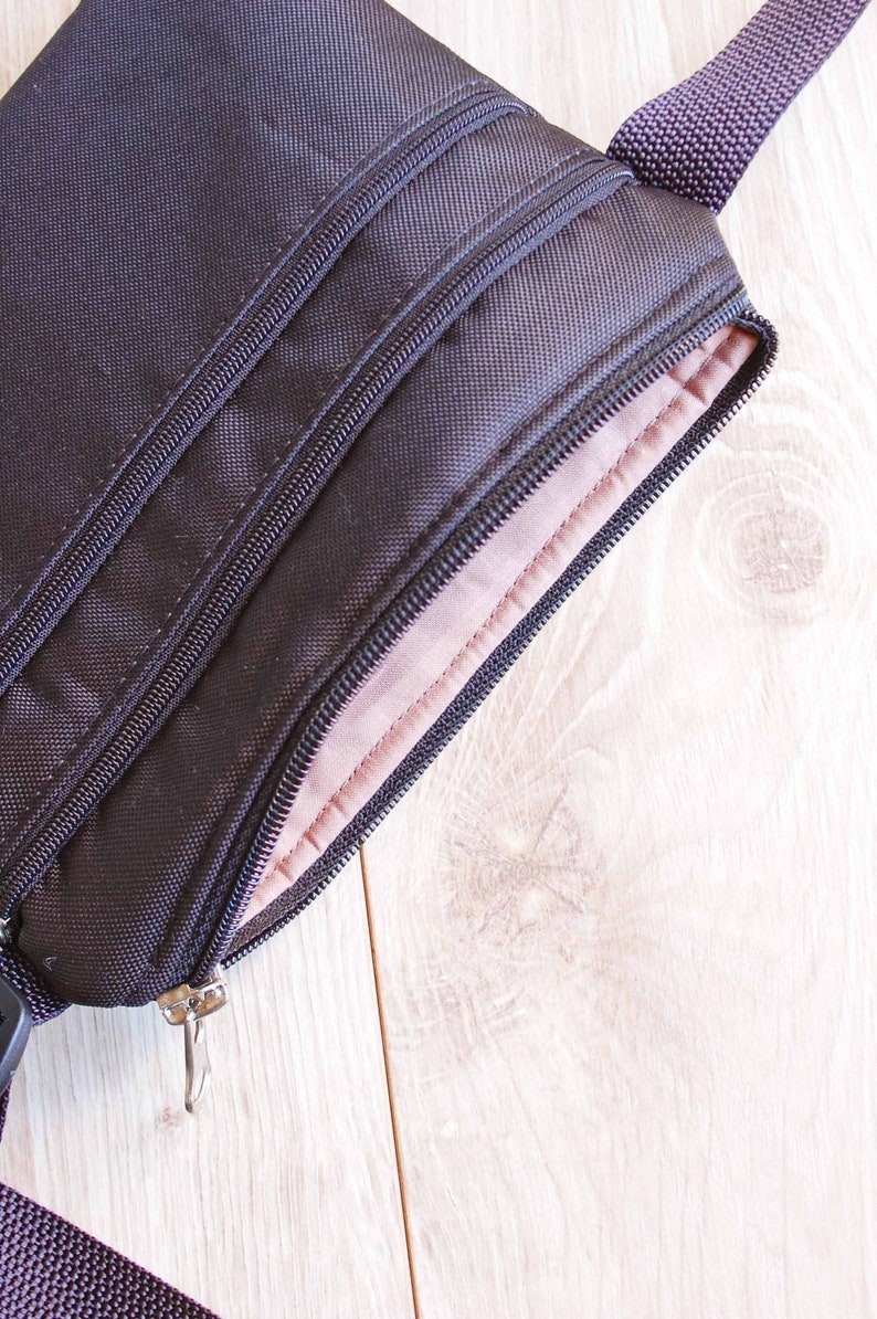 May include: A black zippered pouch with a brown lining. The pouch has a zipper pull and a strap.