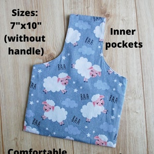 Pode incluir: Uma bolsa de tecido azul com um padr&atilde;o de ovelhas e as palavras "BAA" impressas nela. A bolsa tem uma al&ccedil;a confort&aacute;vel e bolsos internos. A bolsa mede 17,8 cm por 25,4 cm sem a al&ccedil;a.