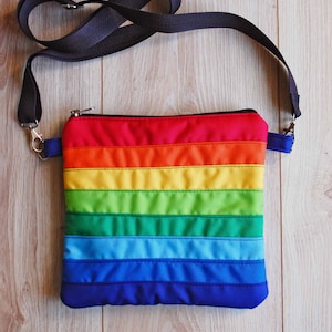 May include: A rainbow striped crossbody bag with a black adjustable strap. The bag has a zipper closure and is made of a quilted fabric.