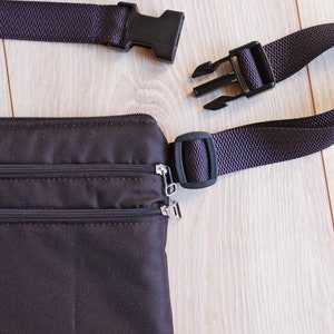 May include: A brown fanny pack with two zippered compartments and a black adjustable strap with two plastic buckles.