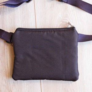 May include: A black fanny pack with a zipper closure and adjustable straps. The straps are made of a dark purple fabric and have black plastic buckles.