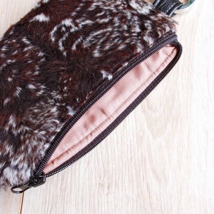 K&ouml;nnte beinhalten: Eine braune und wei&szlig;e Tasche aus Kunstfell mit Rei&szlig;verschluss und einem silbernen Schl&uuml;sselring.