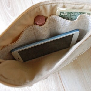 May include: A beige canvas zippered pouch with multiple pockets. The pouch is open and contains a smartphone, a small tube of lip balm, and a one dollar bill.