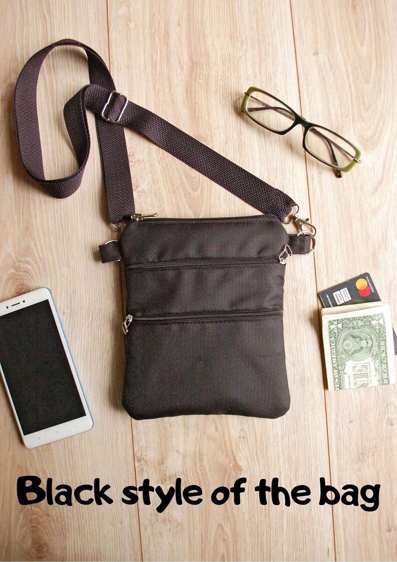 May include: A black crossbody bag with three zippered compartments. The bag has a long adjustable strap and is shown on a wooden surface with a cell phone, glasses, and cash.