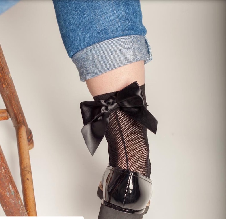 Peut inclure: Chaussettes noires en r&eacute;sille avec un grand n&oelig;ud en satin noir &agrave; la cheville. Les chaussettes sont port&eacute;es avec des chaussures en cuir verni noir.