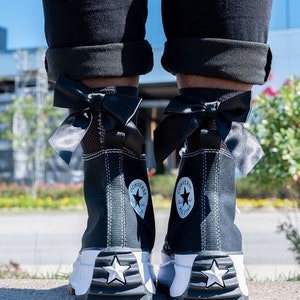 Peut inclure: Des baskets Converse noires montantes avec des &eacute;toiles blanches et un ruban noir nou&eacute; en n&oelig;ud autour de la cheville.