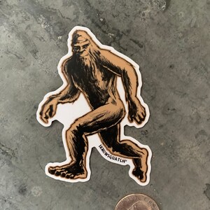 May include: A brown and black sticker of a Bigfoot walking with the text "Knowsquatch" on the bottom.