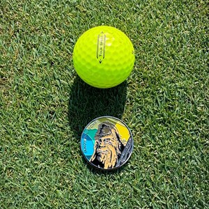May include: A yellow golf ball with the text "Tour Speed" printed on it, and a round metal pin with a colorful design and the text "Know Your Roots" printed on it.