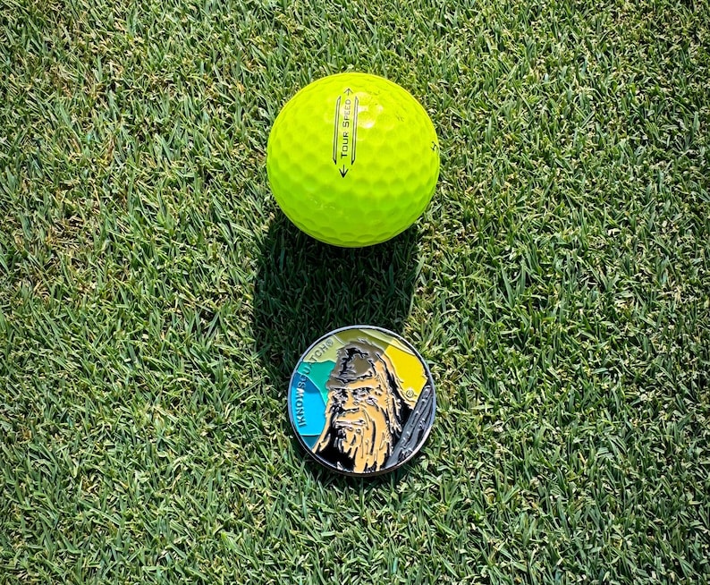 May include: A yellow golf ball with the text "Tour Speed" printed on it, and a round metal pin with a colorful design and the text "Know Your Roots" printed on it.