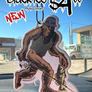 May include: An air freshener with a Bigfoot design, holding a fishing rod and a fish. The air freshener has the text "Black Ice" and "Fishing Strider". The price is $4.00. The word "NEW" is also visible.