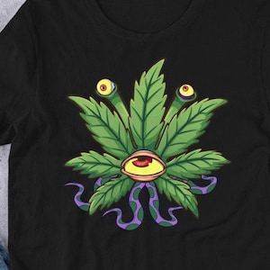Pode incluir: Camiseta preta com um design de folha de maconha verde. A folha tem um único olho no centro e dois olhos menores nos caules.